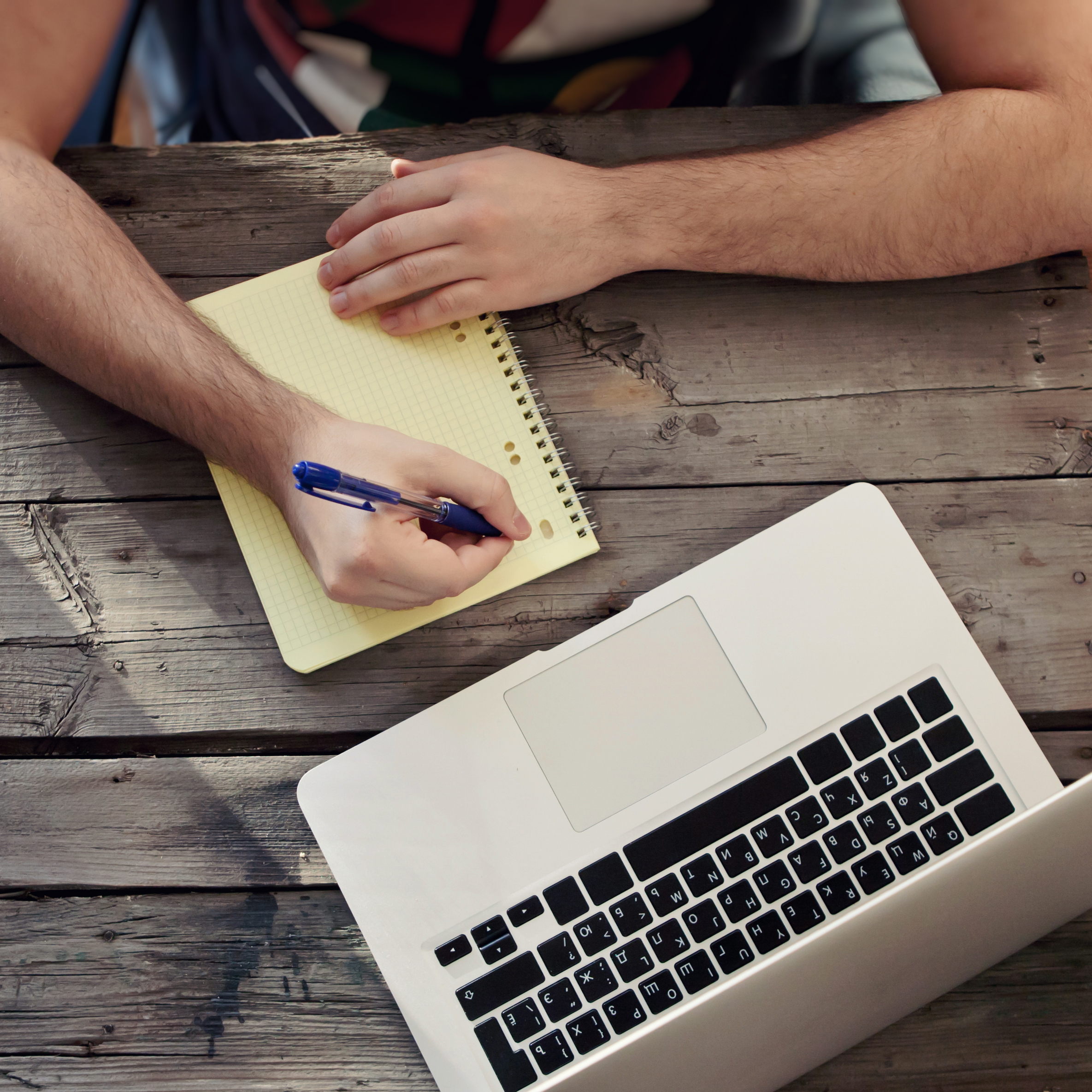 person writing on a yellow page in front of laptop