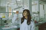 Student in a lab in a white lab coat looking at a bacterial plate